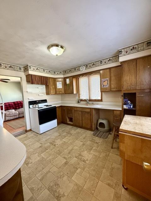 kitchen featuring light countertops, electric range, brown cabinetry, and a sink