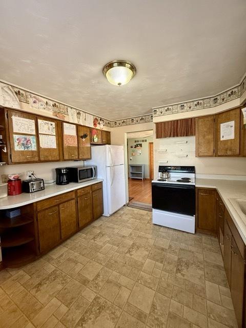 kitchen featuring brown cabinetry, electric range oven, stainless steel microwave, freestanding refrigerator, and light countertops