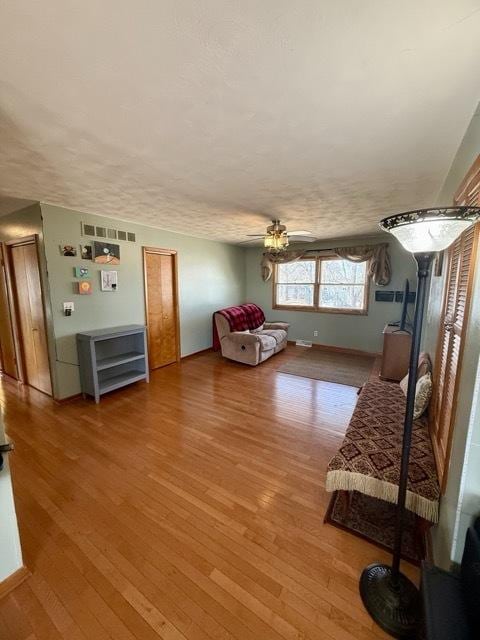 living area featuring light wood-style flooring, visible vents, ceiling fan, and baseboards