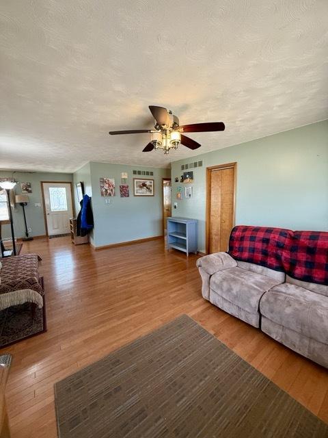 living area featuring visible vents, ceiling fan, a textured ceiling, wood finished floors, and baseboards