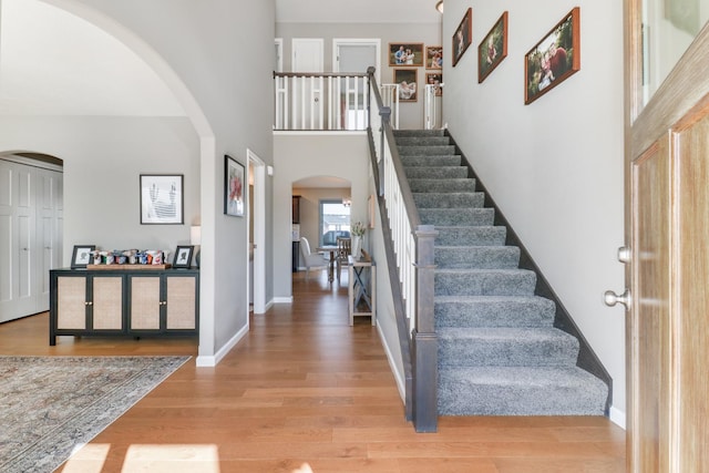 foyer with arched walkways, baseboards, a high ceiling, and wood finished floors