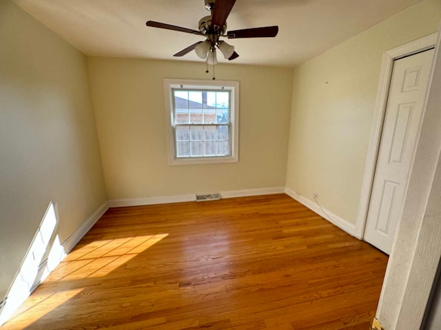 empty room with ceiling fan, wood finished floors, visible vents, and baseboards