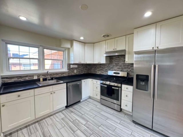 kitchen with dark countertops, backsplash, appliances with stainless steel finishes, a sink, and under cabinet range hood