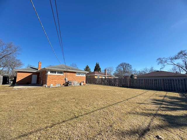 back of property with brick siding, fence, a chimney, and a lawn