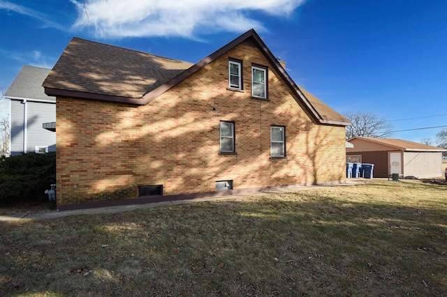 view of home's exterior with a shingled roof, brick siding, and a lawn