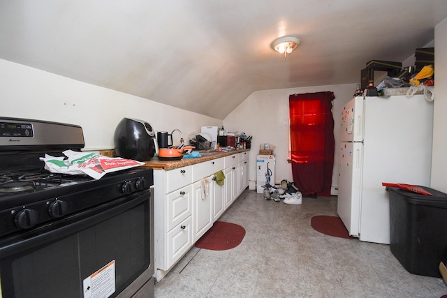 kitchen with stainless steel gas stove, freestanding refrigerator, vaulted ceiling, light floors, and white cabinetry