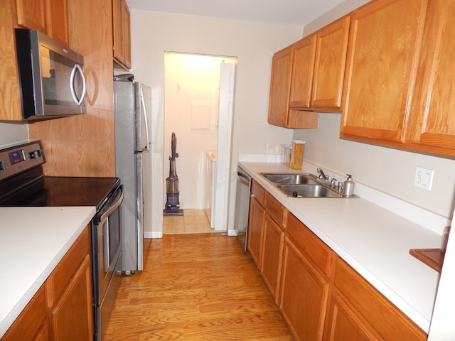 kitchen with light countertops, appliances with stainless steel finishes, a sink, and light wood-style flooring