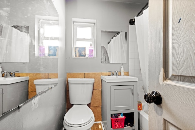 bathroom with toilet, wainscoting, vanity, and tile walls