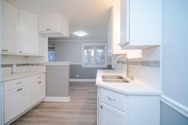 kitchen with light wood-type flooring, light countertops, white cabinetry, and a sink