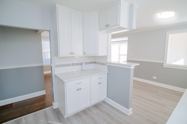 kitchen featuring baseboards, light countertops, light wood-type flooring, and white cabinets