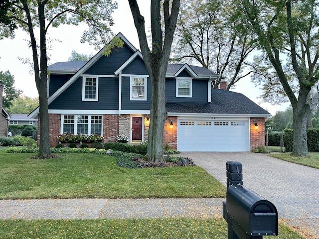 view of front of house featuring an attached garage, a front yard, decorative driveway, and brick siding