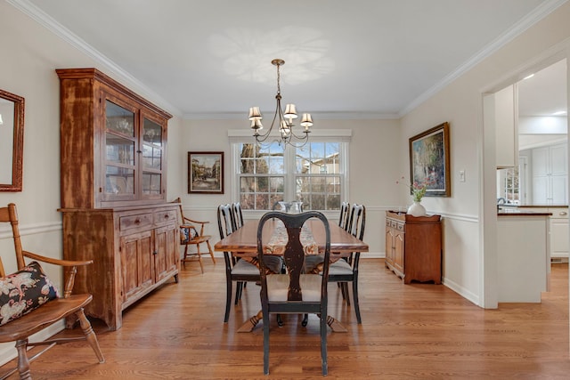 dining room with light wood-style floors, baseboards, ornamental molding, and an inviting chandelier
