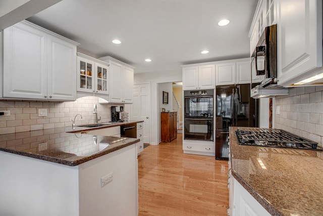 kitchen featuring light wood-style floors, white cabinetry, a sink, dark stone countertops, and black appliances