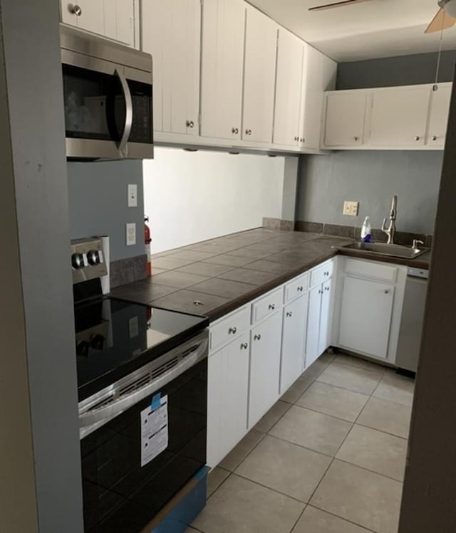 kitchen with appliances with stainless steel finishes, white cabinetry, a sink, and light tile patterned floors