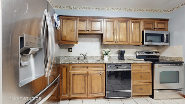 kitchen with stainless steel appliances, brown cabinets, a sink, and light stone countertops