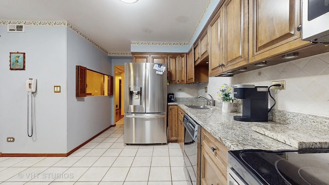 kitchen with light stone counters, brown cabinets, stainless steel appliances, light tile patterned flooring, and a sink