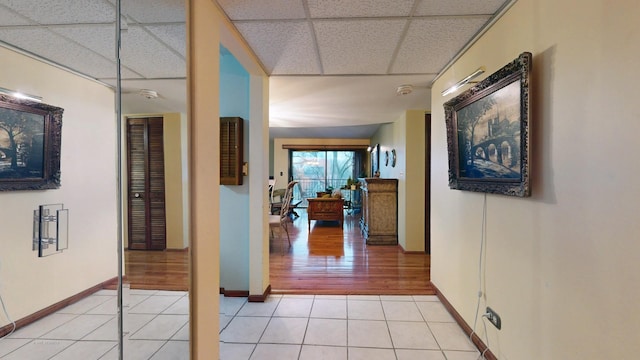 corridor with a paneled ceiling, light tile patterned flooring, and baseboards