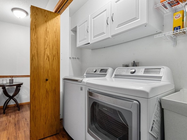 washroom featuring cabinet space, a sink, wood finished floors, washer and dryer, and baseboards