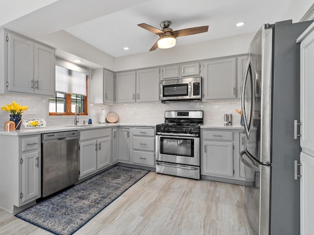 kitchen featuring stainless steel appliances, gray cabinets, light countertops, light wood-style flooring, and a sink