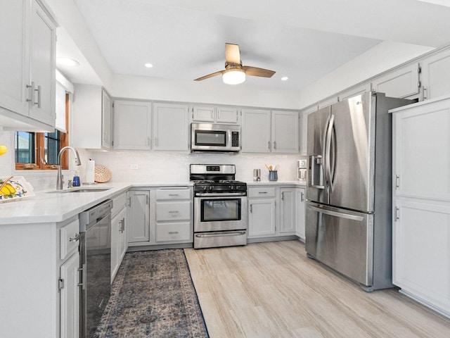 kitchen featuring stainless steel appliances, a sink, light countertops, backsplash, and light wood finished floors