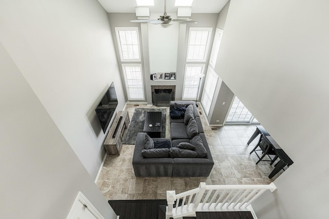 living room with ceiling fan, a fireplace, a towering ceiling, and baseboards