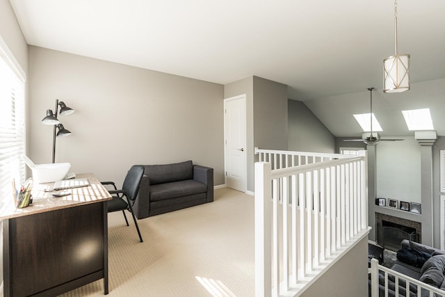 office area featuring lofted ceiling with skylight, a fireplace, baseboards, and light colored carpet