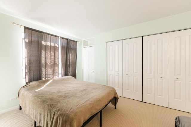 bedroom featuring multiple closets, light colored carpet, and baseboards