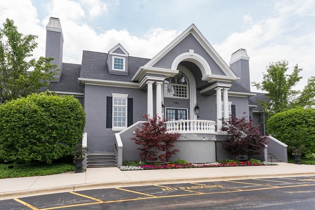 neoclassical / greek revival house featuring a shingled roof, a chimney, and stucco siding