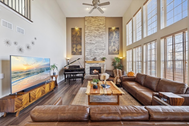 living room featuring a ceiling fan, visible vents, wood finished floors, and a stone fireplace