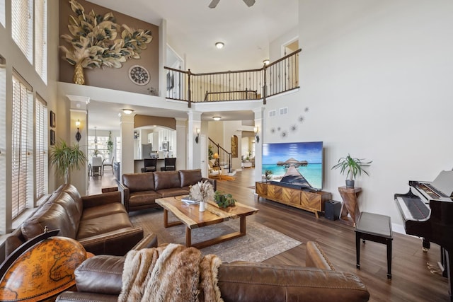 living room with ceiling fan, wood finished floors, visible vents, stairs, and ornate columns