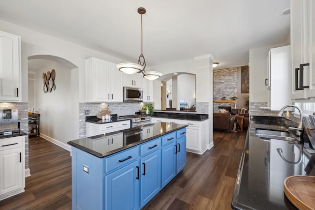 kitchen featuring arched walkways, dark countertops, appliances with stainless steel finishes, a sink, and blue cabinets