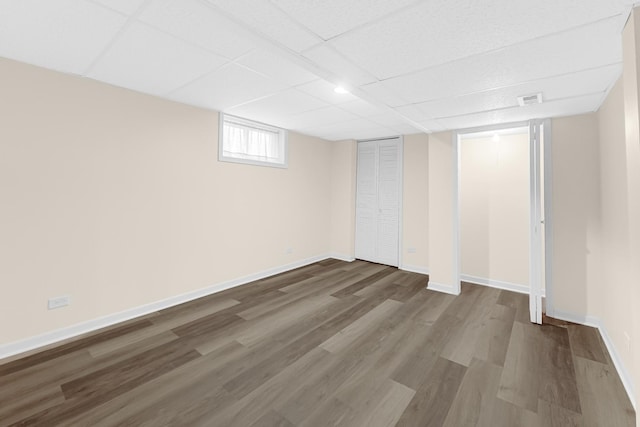 basement featuring a paneled ceiling, visible vents, baseboards, and wood finished floors