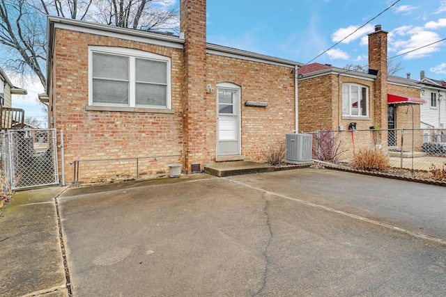 back of house with a gate, brick siding, fence, and central air condition unit