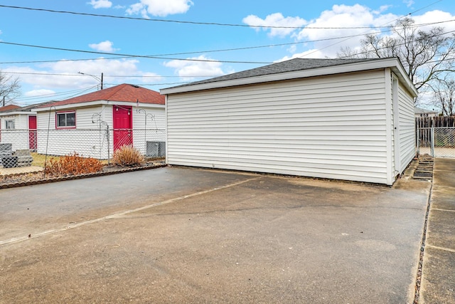 view of side of home featuring an outbuilding, roof with shingles, and fence