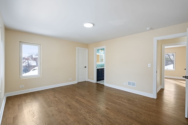 empty room with dark wood-style flooring, visible vents, and baseboards