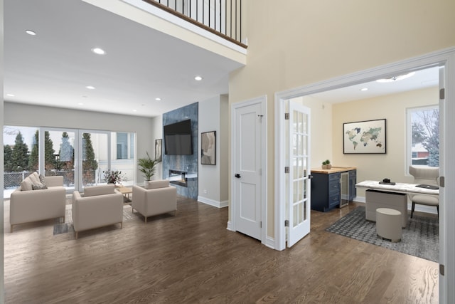 living area with recessed lighting, a high ceiling, a high end fireplace, baseboards, and dark wood-style floors