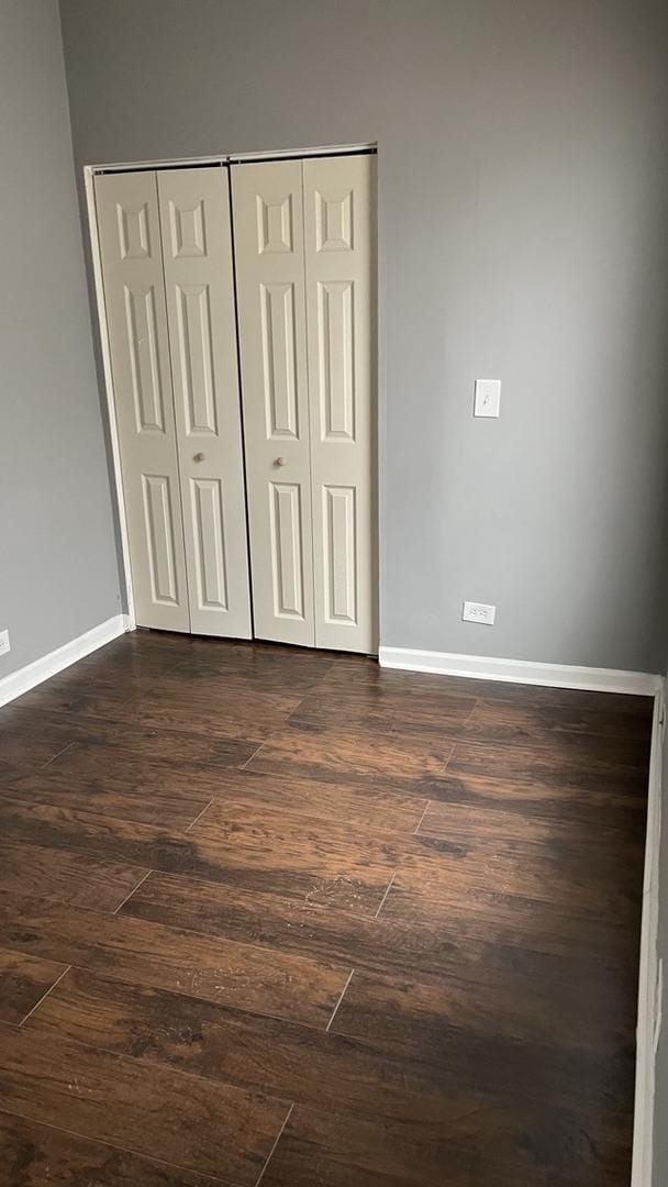 unfurnished bedroom with dark wood-type flooring, a closet, and baseboards