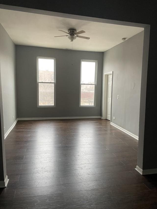 empty room featuring dark wood-style flooring, a healthy amount of sunlight, ceiling fan, and baseboards