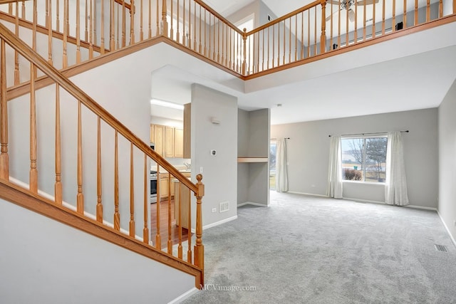 unfurnished living room with carpet floors, a high ceiling, visible vents, baseboards, and stairway