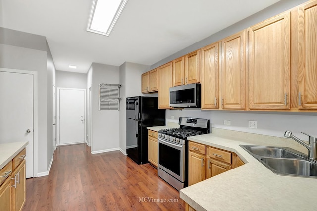 kitchen featuring stainless steel appliances, light countertops, light brown cabinets, a sink, and wood finished floors