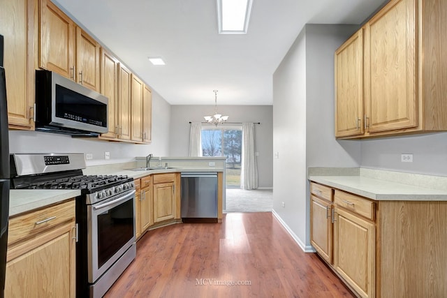 kitchen with appliances with stainless steel finishes, light countertops, a sink, and light brown cabinetry