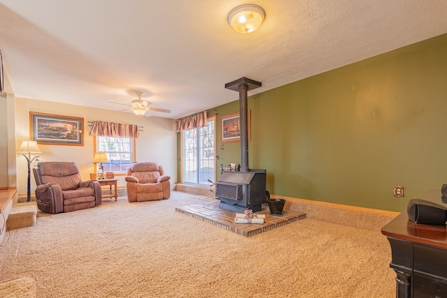 living area with a textured ceiling, a wood stove, carpet, and ceiling fan