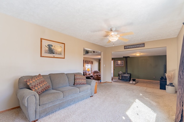 carpeted living area featuring a wood stove, a ceiling fan, baseboards, and a textured ceiling