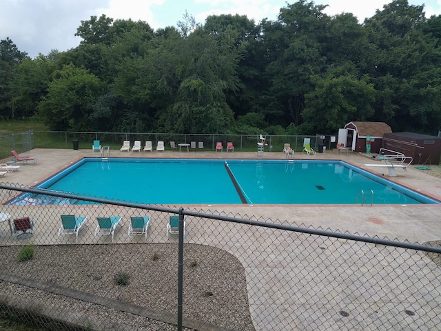 community pool with a storage shed, a patio area, fence, and an outdoor structure