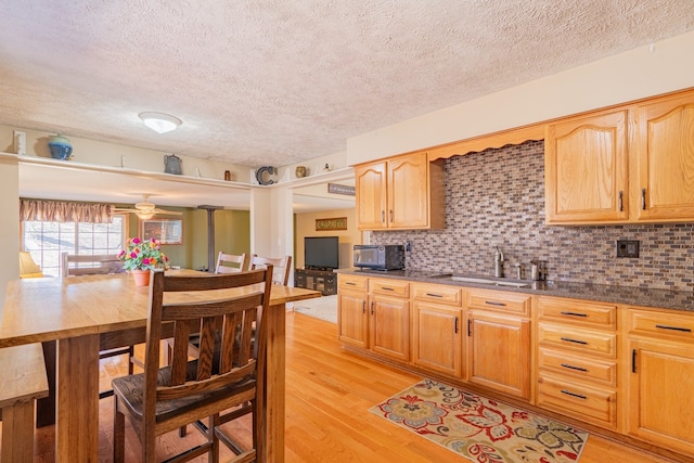 kitchen featuring a sink, decorative backsplash, black microwave, dark countertops, and light wood-type flooring