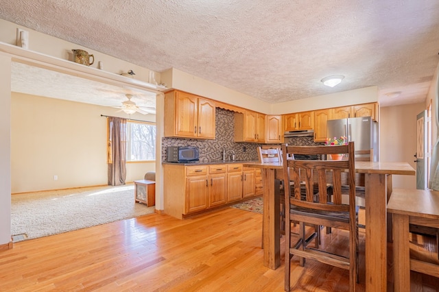 kitchen featuring light wood-style flooring, under cabinet range hood, backsplash, freestanding refrigerator, and black microwave