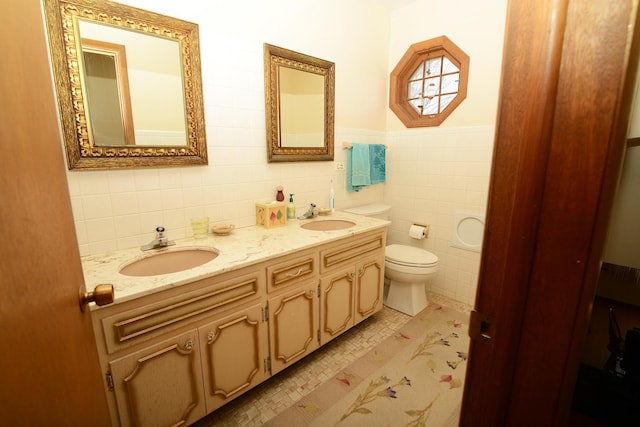 bathroom with double vanity, toilet, tile walls, and a sink