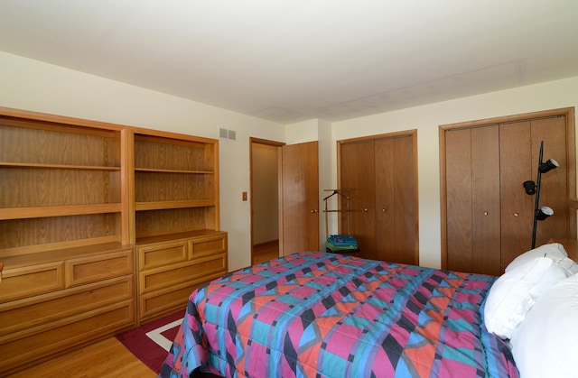 bedroom with visible vents, light wood-style flooring, and multiple closets