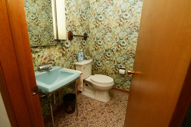 half bathroom featuring wallpapered walls, toilet, baseboards, and a sink