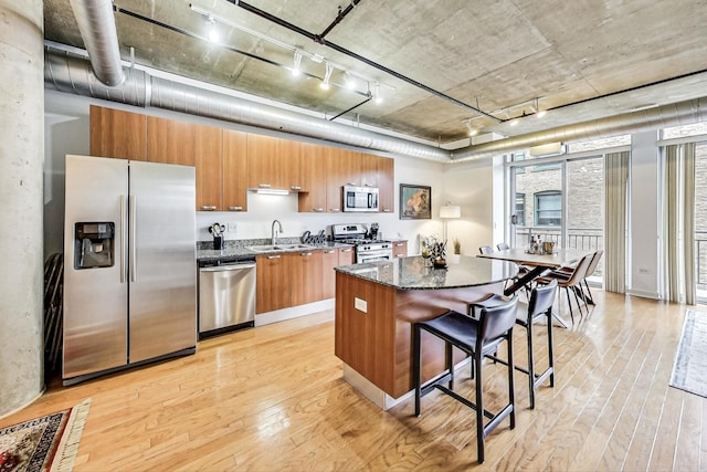 kitchen with a center island, light wood-type flooring, a kitchen breakfast bar, brown cabinetry, and stainless steel appliances